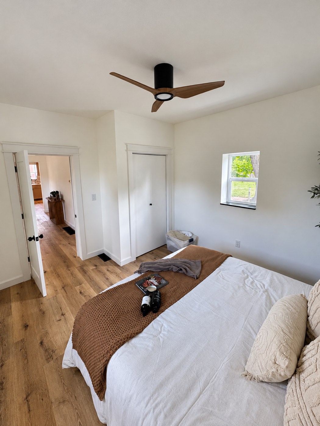 The finished bedroom on the closet side, with a bed, plank flooring, white trim and doors and a ceiling fan