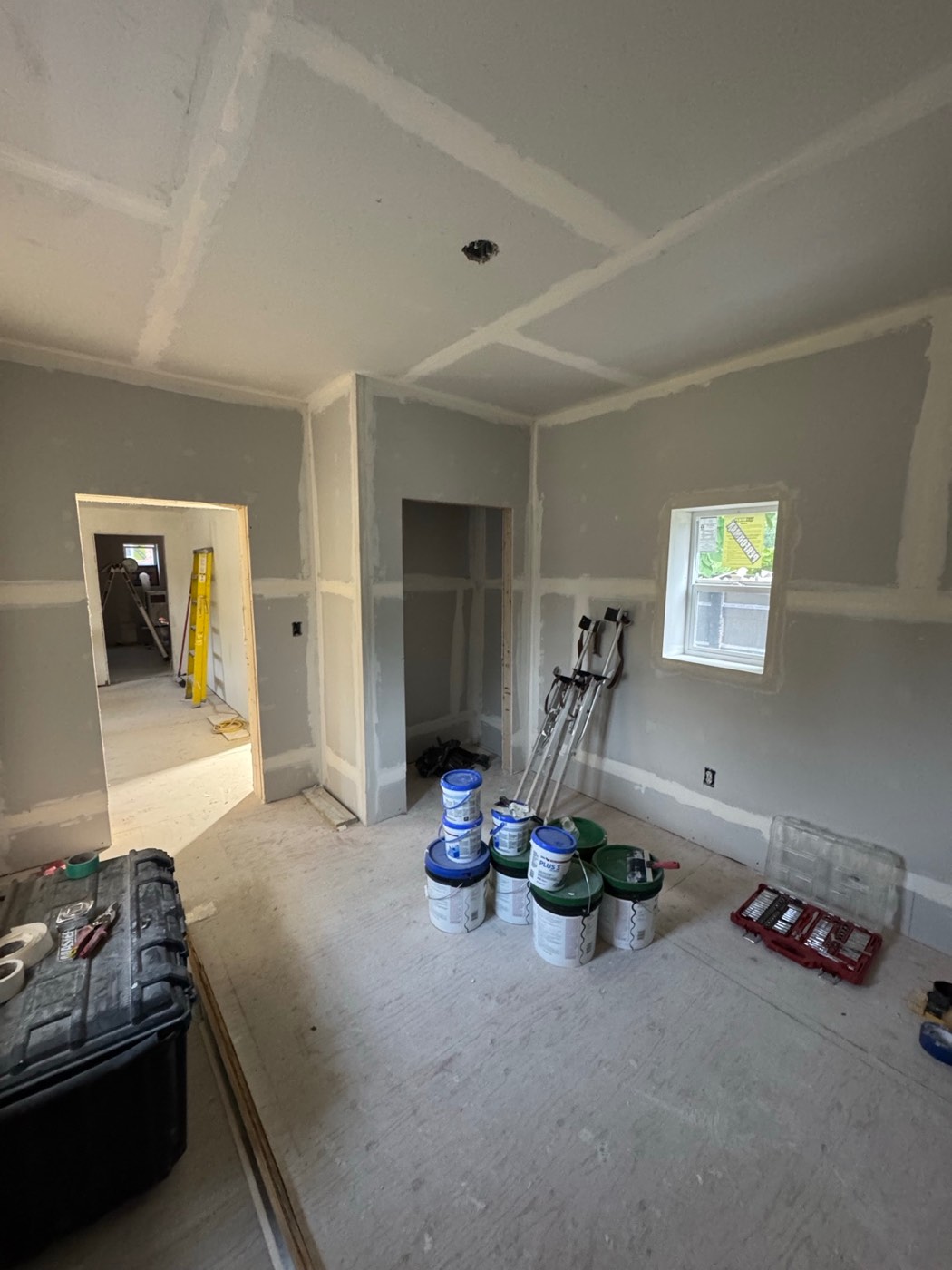 The same bedroom during renovation from another angle, with drywall stilts, buckets of joint compound and the closet opening