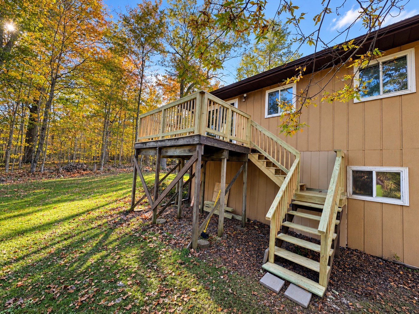 Raised backyard deck with new wood railings, balusters and staircase beside tan siding