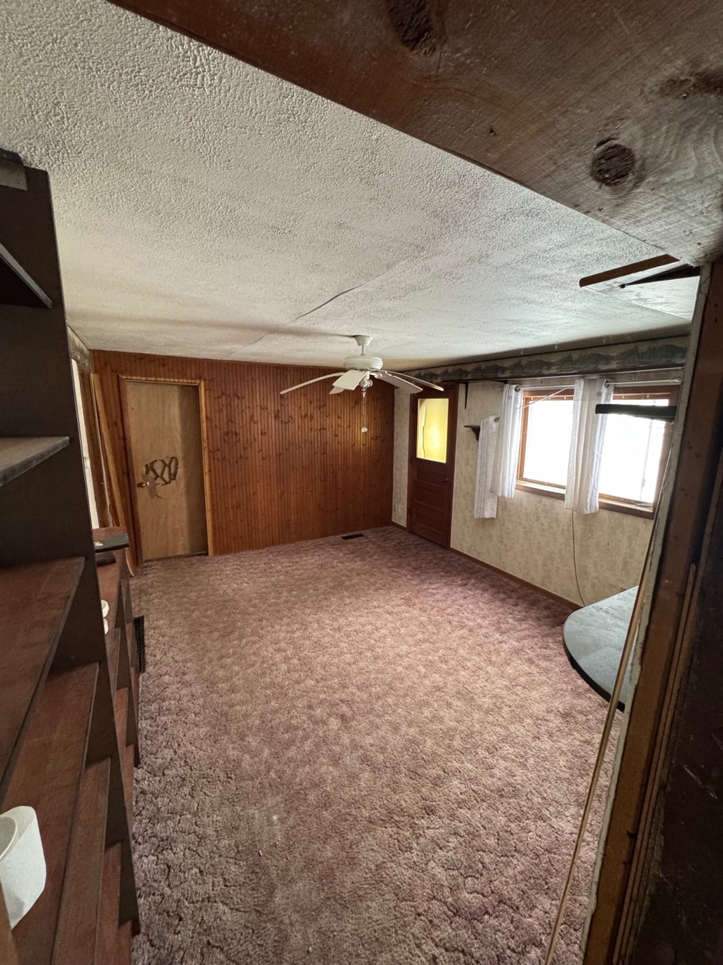 Original living room with wood paneling, wallpaper, a textured ceiling, a ceiling fan and worn carpet