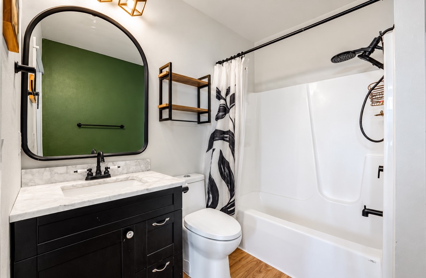 Bathroom with black vanity, marble-look top, arched mirror and tub surround