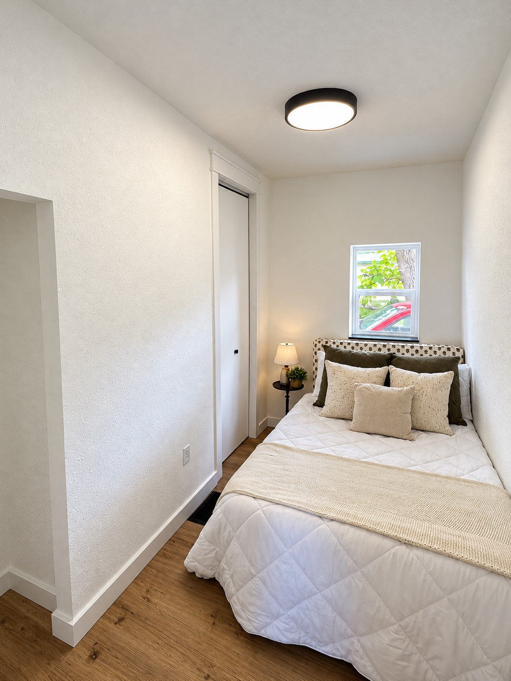 Finished small bedroom with a window above the bed, a white bifold closet door, a flush-mount light and plank flooring