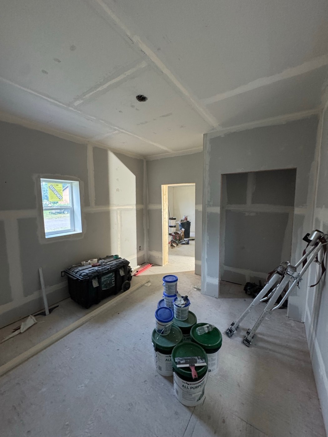 Bedroom during renovation with taped and mudded drywall, a window on the left wall, a doorway and a closet opening