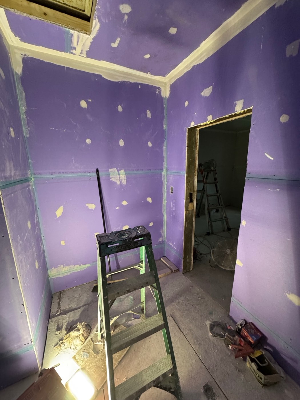 The same bathroom during renovation, looking toward the door, with purple drywall hung and the first coat of joint compound applied